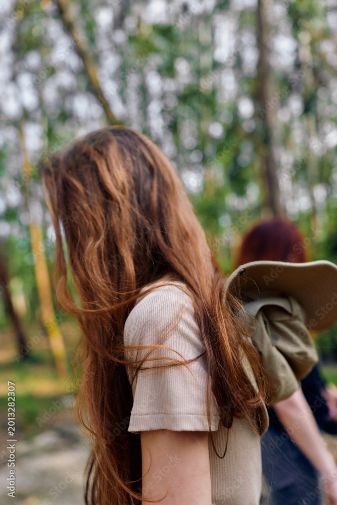 Fototapeta premium Woman with long hair in forest nature, casual backpack and walk with friend, side portrait and redhead profile in dappled daylight among trees and green woodland background.