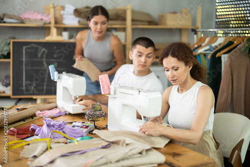 Multiethnic participants in coterie practice sewing, chatting, work textile and paper dress pattern. People while away time among like-minded people. Retraining, profession change and training.