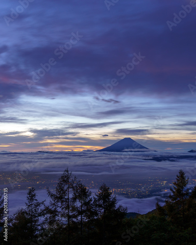 Breathtaking pre-dawn view of Mount Fuji and the glittering city lights of Kofu Basin from Mount Amari, Yamanashi, Japan.