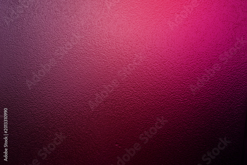 Fotografia Magenta and pink gradient light on a dark bumpy textured surface