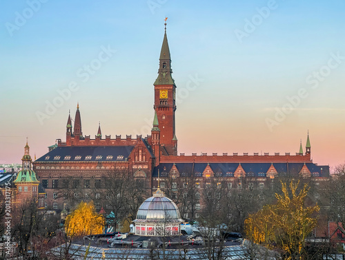 Copenhagen, Denmark - December 31, 2025: City hall under Christmas winter sunset light against ligh blue sky. Tivoli Gardens in front