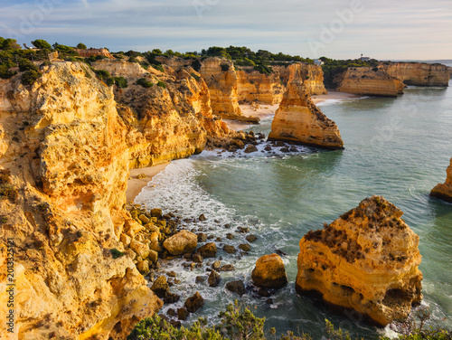 Sunrise view of Praia da Marinha beach in Algarve, Portugal, with golden cliffs, sea stacks, Atlantic waves, turquoise water, and a rocky cove.
