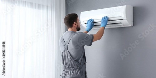 HVAC technician wearing gloves inspecting wall-mounted air conditioner unit indoors, concept for home appliance repair, climate control maintenance and professional service advertising
