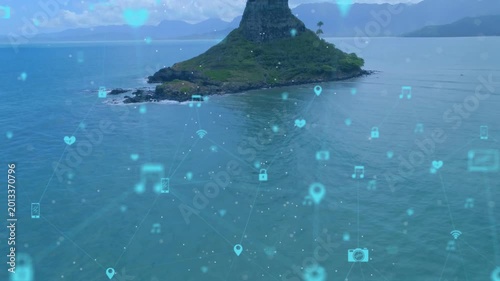 Drone pulling back over sea, island centering, hologram icons forming network to show connectivity