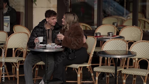 A young couple is sitting at an outdoor in Paris France They are drinking coffee talking and laughing The scene captures a romantic date in a classic French setting The man and woman appear to be enjo