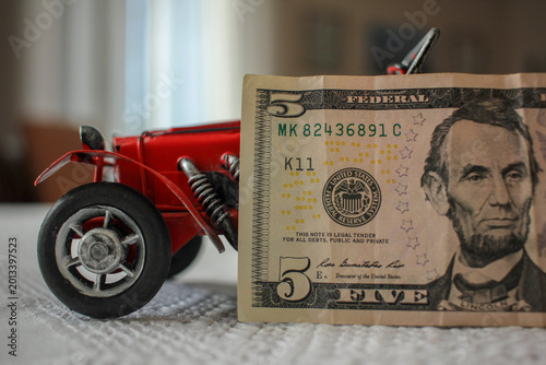 Vintage classic car model with a five dollar bill, concept of inflation and tangible asset investment.