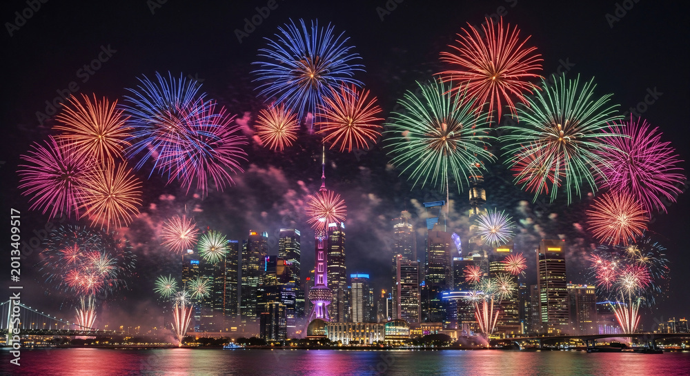 Obraz premium Vibrant Fireworks Exploding over a Modern City Skyline and Reflecting Water at Night