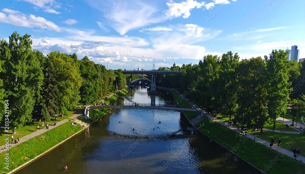Fototapeta premium Aerial View Of A Scenic City Park Canal With Green Trees And Multiple Bridges Under A Bright Blue On A Sunny Summer Day