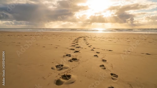 Footprints in the sand leading towards a wooden cross on the beach at sunset. Religious concept reflecting the walk with Jesus Christ during Easter morning light.
