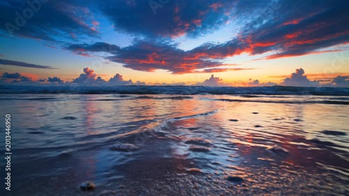 Beach scene at sunset with vibrant colorful clouds reflecting on wet sand