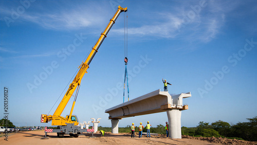 Photos Construction crane lifts concrete bridge section, workers oversee progress on su