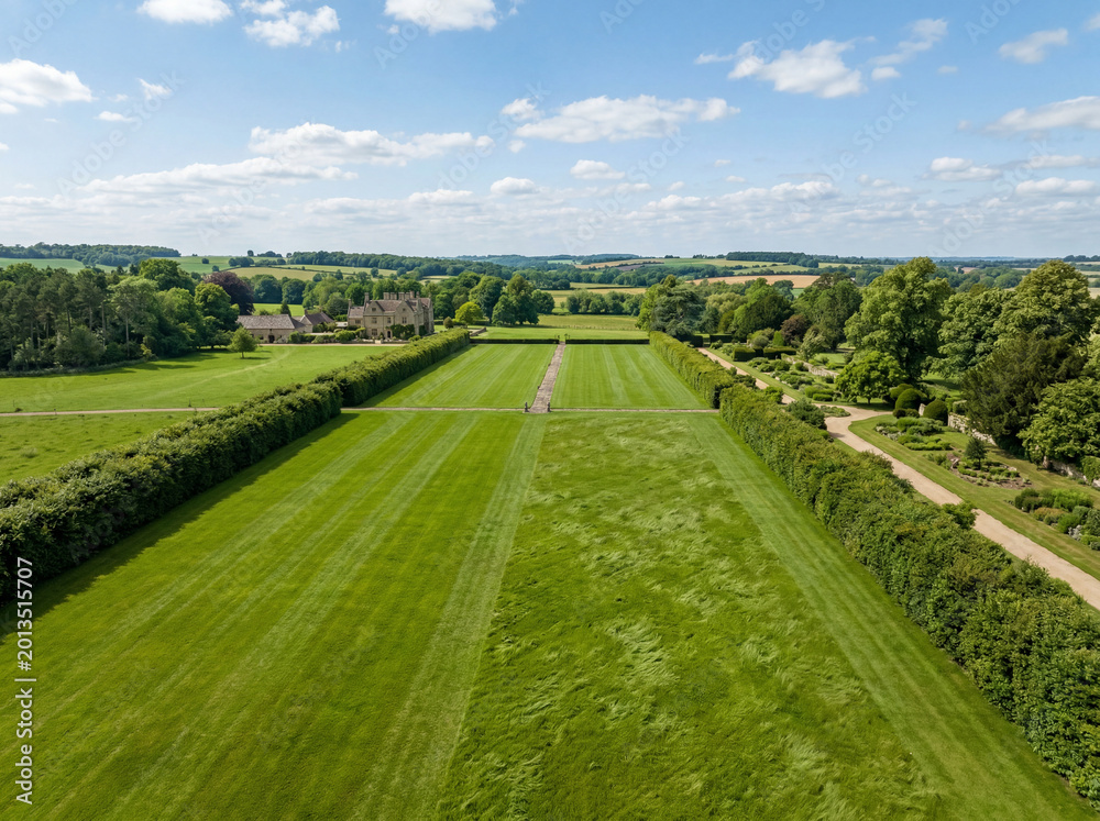 Naklejka premium Expansive green lawn, a meticulously manicured garden landscape with long hedges, perfect for elegant outdoor events and stately home backdrops. Lush grass field for luxury property and estate