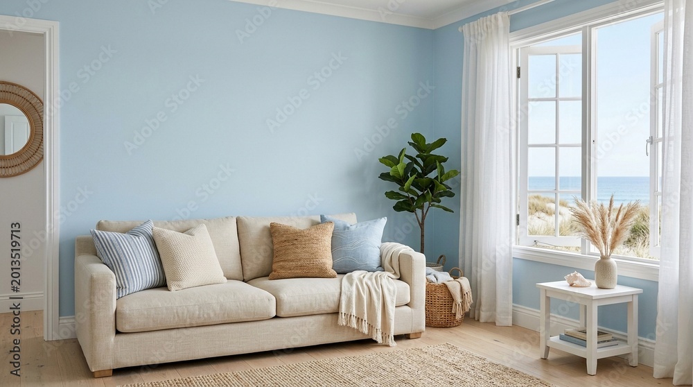 Fototapeta premium Empty Light Blue Wall Mockup in Coastal Interior with Sofa and Pillows. Natural Daylight From a Window. Promotion Background.