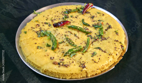 Fluffy yellow dhokla topped with mustard seeds, green chilies, and fresh coriander leaves.