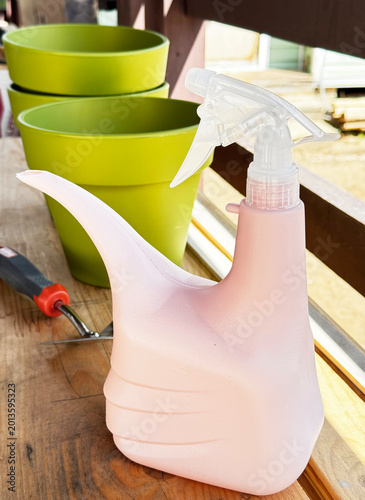 Green pots, a pink watering can, and a garden trowel on a wooden table. Flower seedling growing concept. Side view.