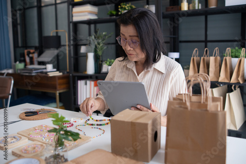 Mature asian woman owner taking online orders with tablet