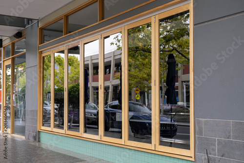 Modern retail shopfront with large glass folding doors and timber frames. Stylish cafe or restaurant exterior with wooden bi-fold glass windows along a paved public walkway