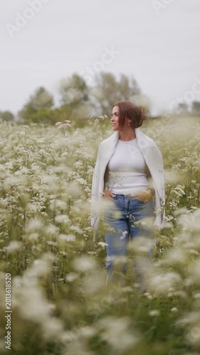 A woman stands thoughtfully in a field of delicate white wildflowers