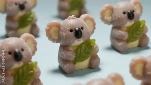 Adorable koala figurines holding eucalyptus leaves, arranged on a light blue surface