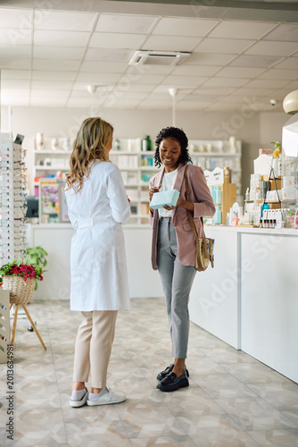Happy black woman talking to pharmacist buying dermal care products in drugstore.