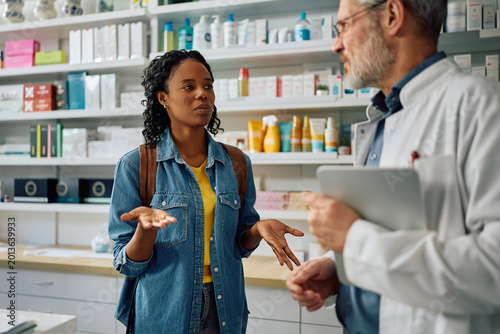 Fotografija Young black woman communicating with pharmacist at drugstore.