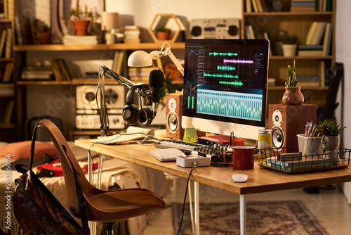 Wide shot of home podcast studio featuring computer editing audio, microphone, headphones, mixer, speakers. Supporting content creation, streaming, remote media production