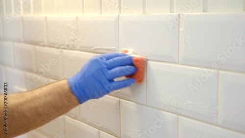 Thoroughly cleaning the grout between tiles. Manually cleaning stains on white tiles. Close-up of a gloved hand cleaning white tiles. A variety of tile cleaning products. The problem of cleaning.