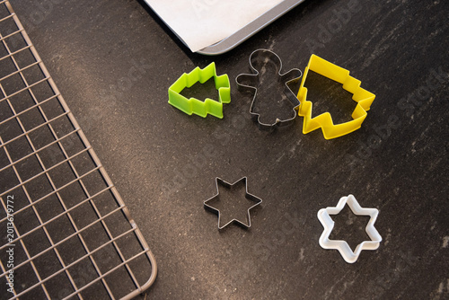 Cookie cutters sitting on dark kitchen counter with green  and  yellow trees, gingerbread, cooling r
