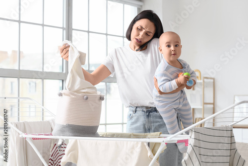 Working mother with her baby talking by mobile phone while hanging laundry on...