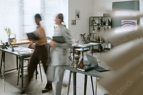 Obraz na plátně Wide shot of diverse businesswomen walking through office carrying folders, creating motion blur and teamwork concept