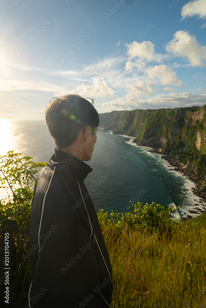 Fototapeta premium Man posing at Manta Point on Nusa Penida, Bali, enjoying tropical ocean landscape and adventure travel atmosphere.
