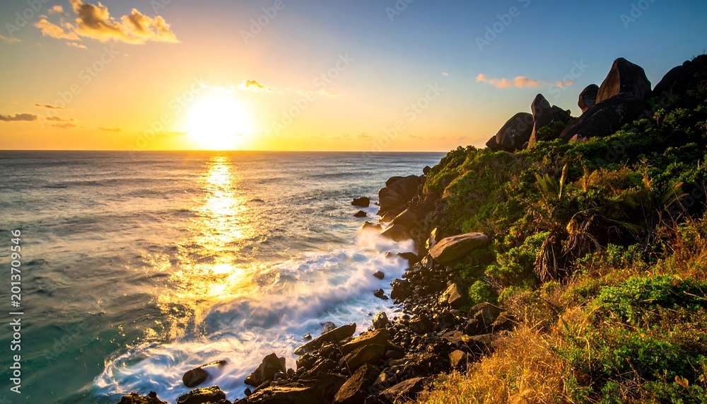 Fototapeta premium Seaside cliff at sunset, with waves crashing on rocks, golden light, blue ocean, and tropical vegetation