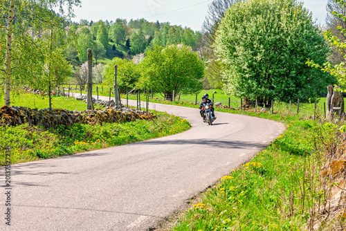 Foto Motorcyclist on winding country road in lush spring landscape
