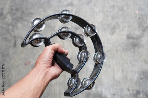 Fotografie A close-up shot of a hand holding a black, crescent-shaped plastic tambourine against a blurred, neutral grey concrete background