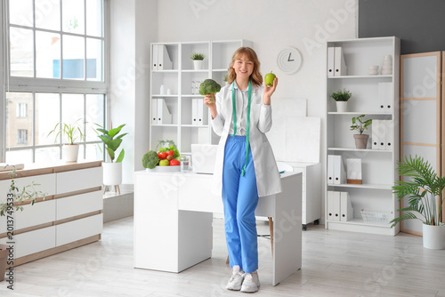 Female nutritionist with broccoli and apple in office