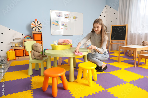Female nursery teacher disinfecting table in kindergarten