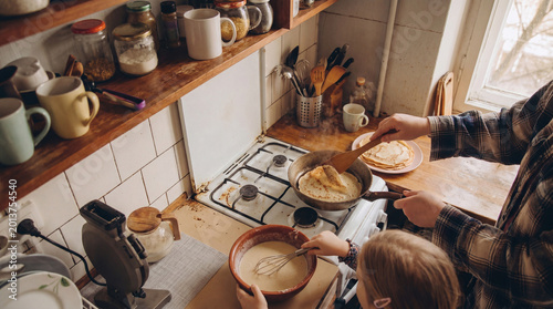 Fotografia High angle view of a parent and child preparing breakfast together, cooking pancakes on a gas stove at home