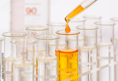 Aus einer Pipette fällt ein Tropfen gelber Flüssigkeit in ein Reagenzglas in einem Labor