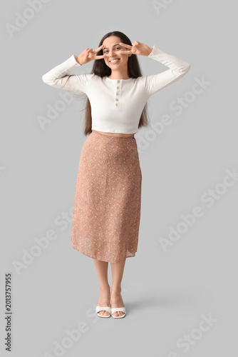 Happy young woman showing victory gestures on grey background
