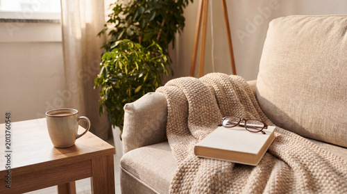 Photos Inviting and cozy living room corner featuring a comfortable sofa with a warm knitted blanket, a book, glasses