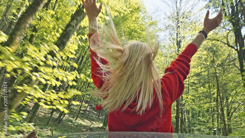 Photos In the heart of a lush, verdant forest, a caucasian woman with flowing blonde hair raises her arms in exhilaration as she hikes through the vibrant greenery of springtime