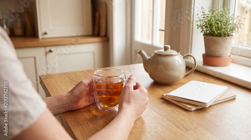 Tableau sur toile Hands holding a warm glass of herbal tea on a rustic wooden kitchen counter, fostering a sense of comfort