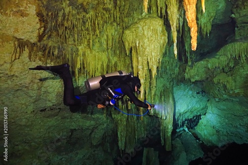 Scuba diver cave explorer in the underwater limestone cave with lamp. Technical cave diving, speleology with stalactites. Diver in the cenote with flashlight, underwater travel photo from scuba trip.