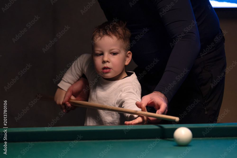 Fototapeta premium Parent teaching young child to play billiards on pool table indoors