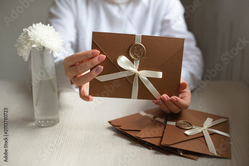 elegant handmade wedding invitation in brown paper with white satin bow in woman hands