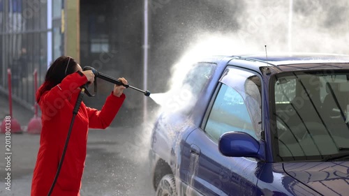 A woman washes her blue car at a self-service car wash. The car wash's high-pressure jet sprays water and rinses away the cleaning foam. 4k footage.