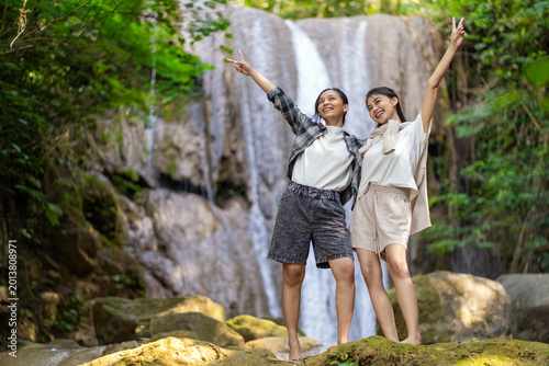 Women standing on rocks raising hands near waterfall