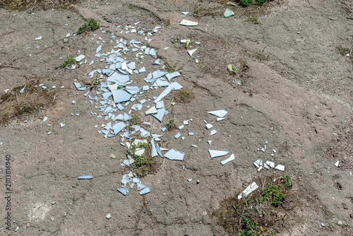 Scattered shards of broken glass lying on cracked asphalt ground with small patches of green grass