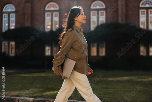 Woman walking across campus holding a laptop