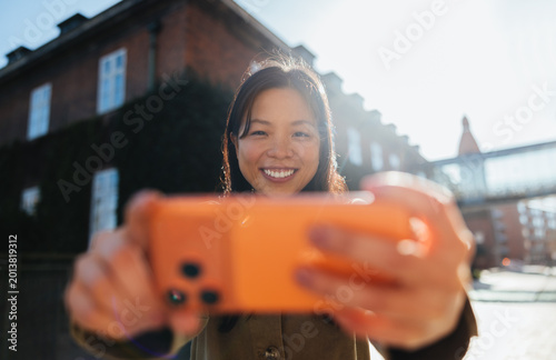 Woman taking a smiling selfie with smartphone outdoors
